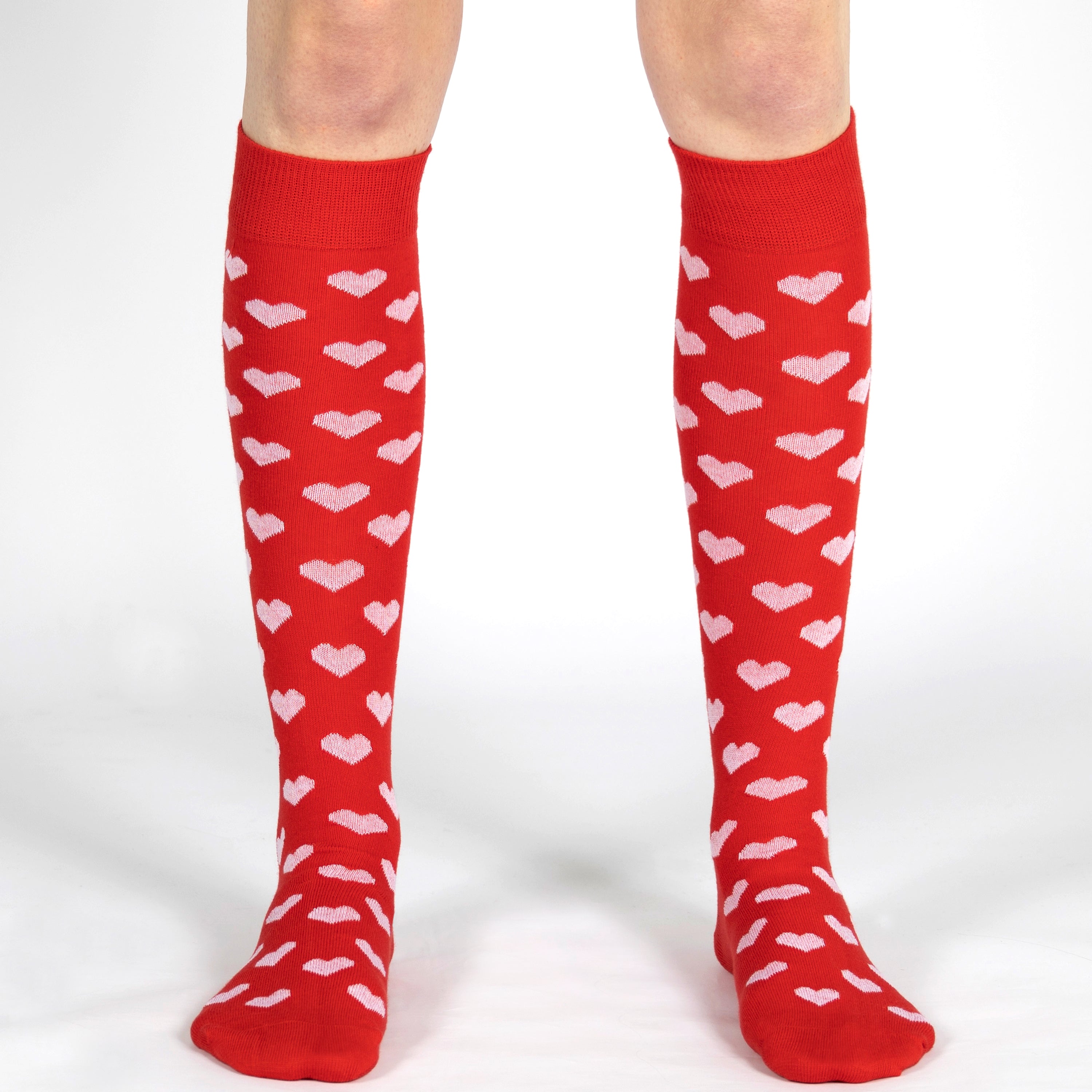 Red knee-high socks with white heart patterns worn by a person on a white background