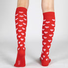 Red knee-high socks with white heart patterns worn by a person on a light gray background