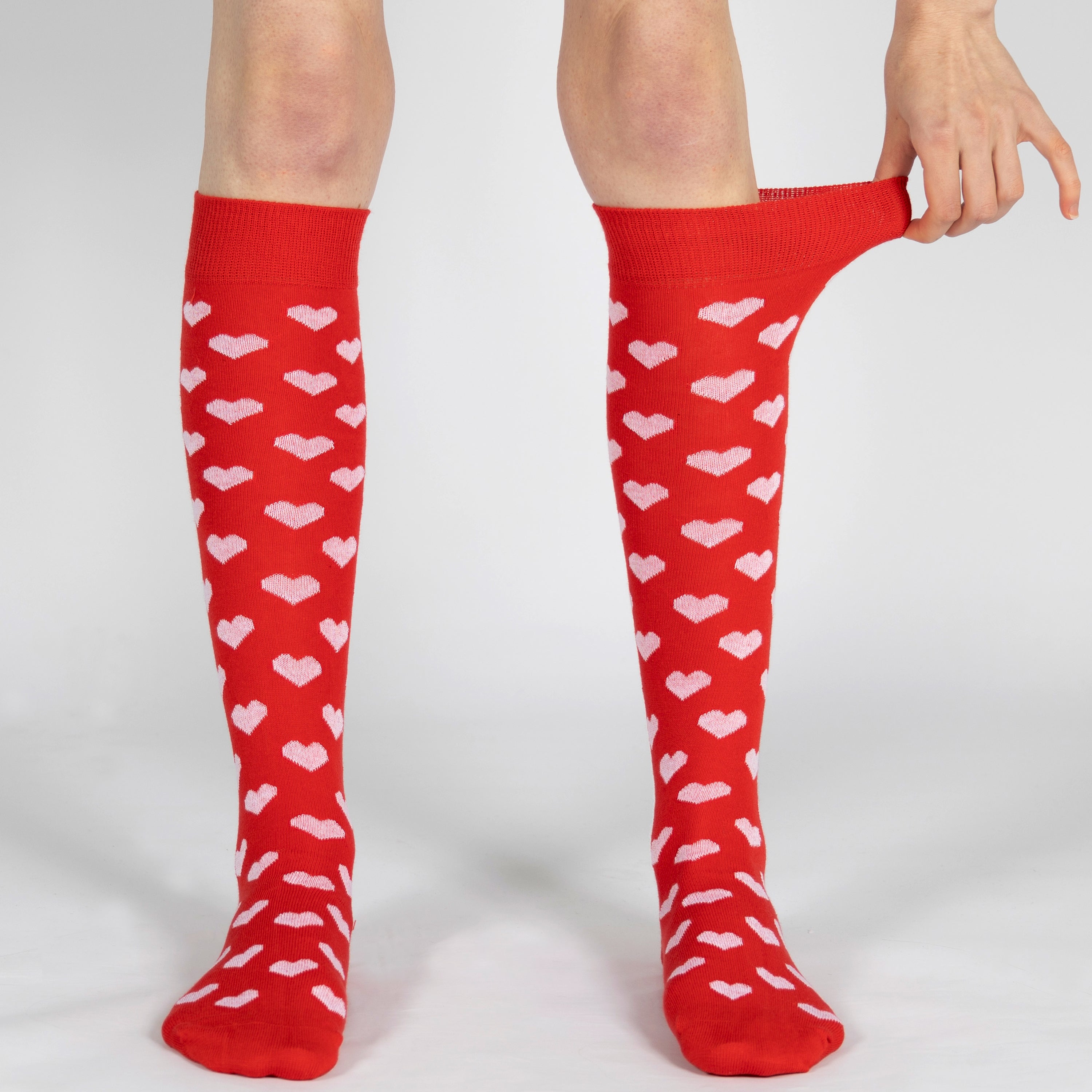 Red knee-high socks with white heart patterns worn by a person on a light gray background