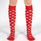 Red knee-high socks with white heart patterns worn by a person on a white background